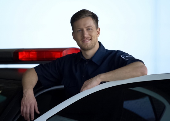 Handsome policeman standing near car and smiling, protection of public safety